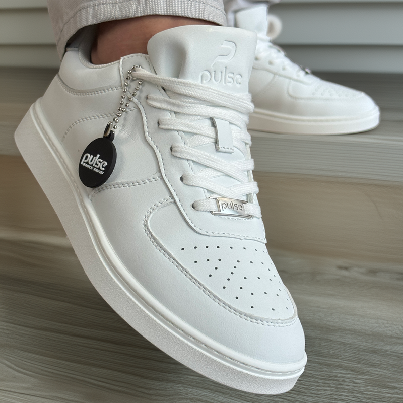 Side view of a white low-top Pulse Dance Shoes dance sneaker with white laces and a black hang tag by timber deck boards